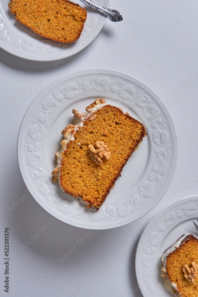 Slices of homemade carrot cake with sugar glaze and walnuts served in three white dishes. Food concept Slices of homemade carrot cake with sugar glaze and walnuts served in three white dishes. Food concept