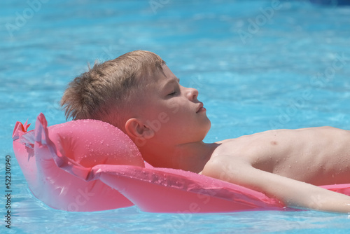 Young child boy relaxing on summer sun swimming on inflatable air mattress in swimming pool during tropical vacations. Summertime activities concept