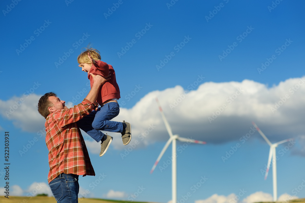 Eco activists man and child on background of power stations for renewable electric energy production. People and windmills. High wind turbines for generation electricity. Green energy Eco activists man and child on background of power stations for renewable electric energy production. People and windmills. High wind turbines for generation electricity. Green energy