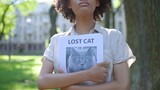 Young woman holding missing cat posters in hands, looking for her lost pet in park