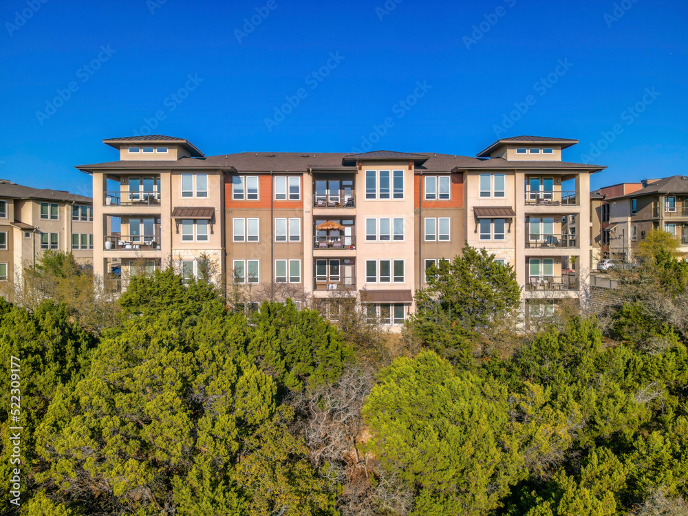 Austin, Texas- Apartment building with balconies and picture windows on top of a slope with trees