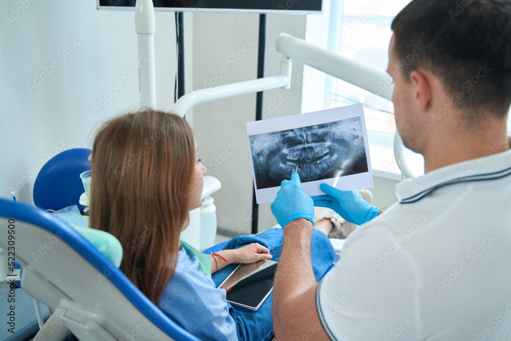 Dentist demonstrating caries on dental radiograph to female patient Dentist demonstrating caries on dental radiograph to female patient