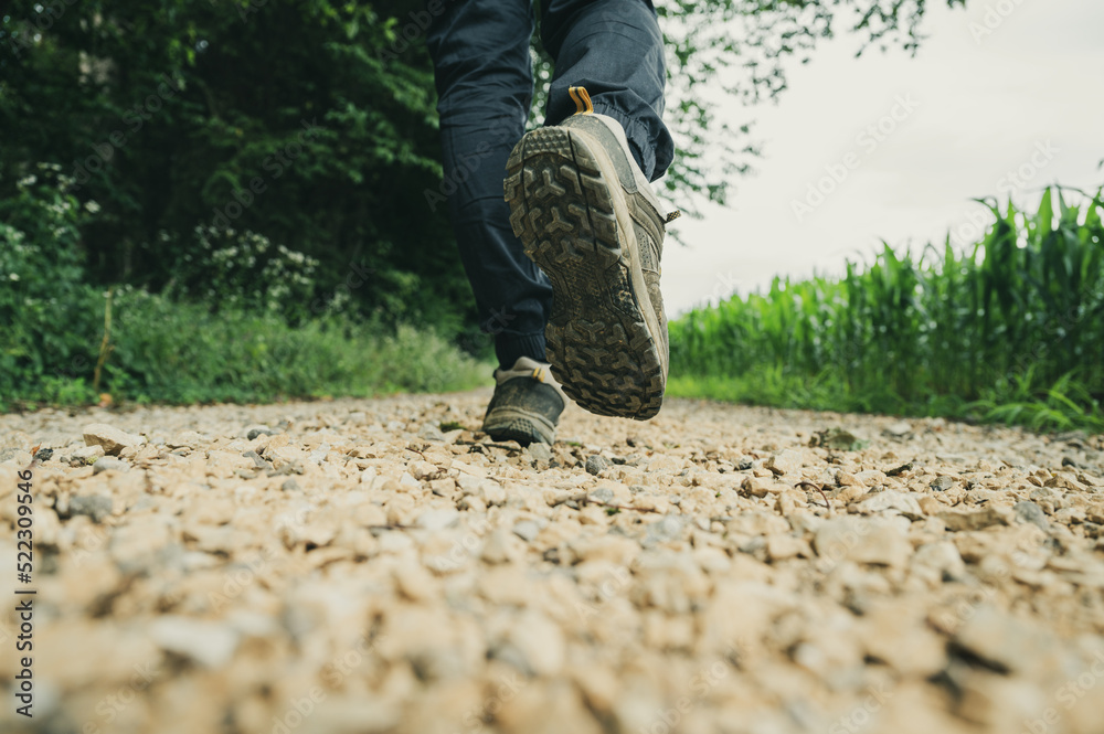 Low angle view of a male legs in hiking boots walking on a gravel country road Low angle view of a male legs in hiking boots walking on a gravel country road
