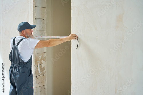 Εκτύπωση καμβά Builder in overalls measures width of doorway with tape measure