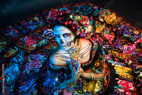 catrina woman dressed in a mexican chiapas costume with a black background pink rebozo and skull and bones makeup on her hands