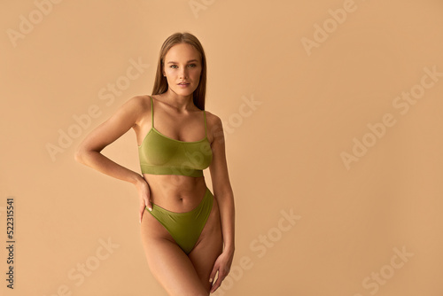  Beautiful athletic tanned woman in green underwear posing on a beige background.