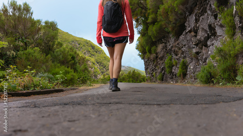 Fototapeta Naklejka Na Ścianę i Meble -  A young woman hiking on a mountain road surrounded by vegetation