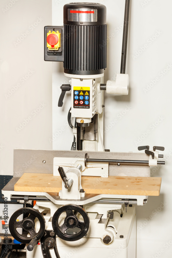 Industrial electric vertical milling machine close-up on a beige background.