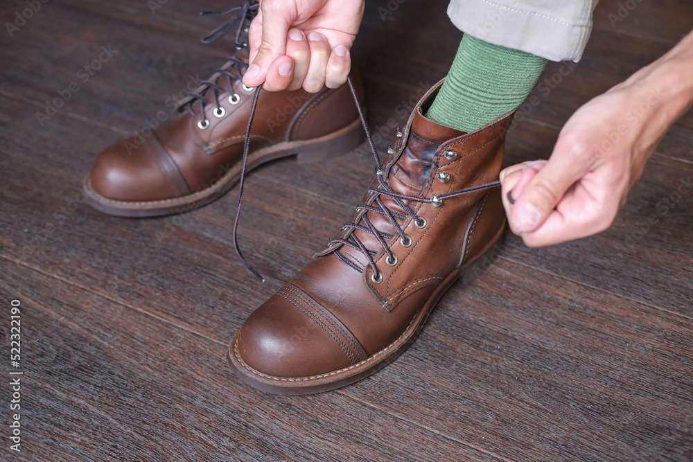 close up feet of men who tying shoelaces on new  leather brown work boot