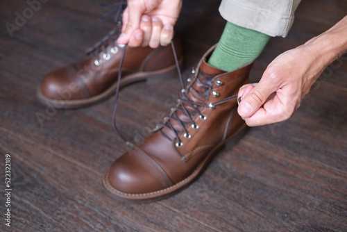 person tying laces of leather brown boots on wooden floor, close-up