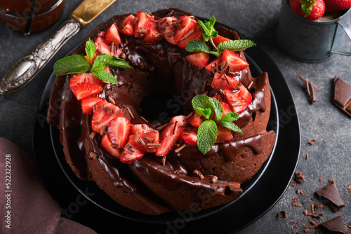 Dark Chocolate Bundt Cake with Ganache Icing and strawberry on dark stone or concrete table background. Festive cake. Selective focus