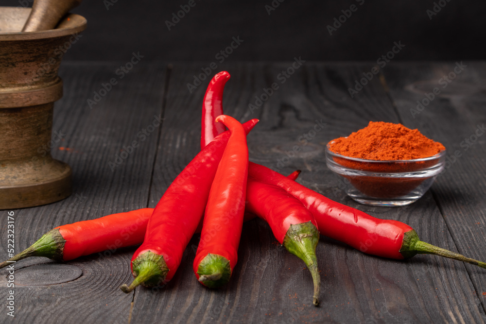 raw and ground chili peppers and a mortar on wooden background