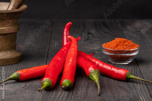 raw and ground chili peppers and a mortar on wooden background