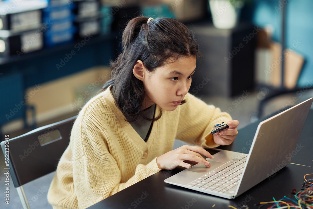 Portrait of young Asian girl using laptop in engineering class and programming robot, copy space Portrait of young Asian girl using laptop in engineering class and programming robot, copy space