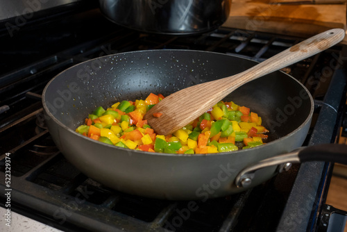Close up, selective focus on diced bell peppers cooking in a large skillet on a gas stove top