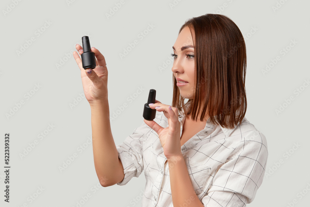 Beautiful young woman serious looking sideways holding bottles of nail varnish. Beauty portrait of brunette girl Beautiful young woman serious looking sideways holding bottles of nail varnish. Beauty portrait of brunette girl