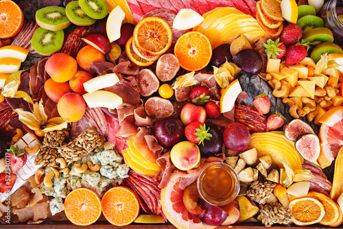 assorted fruits, berries, cheese, sausage, snacks and honey on a tray. 