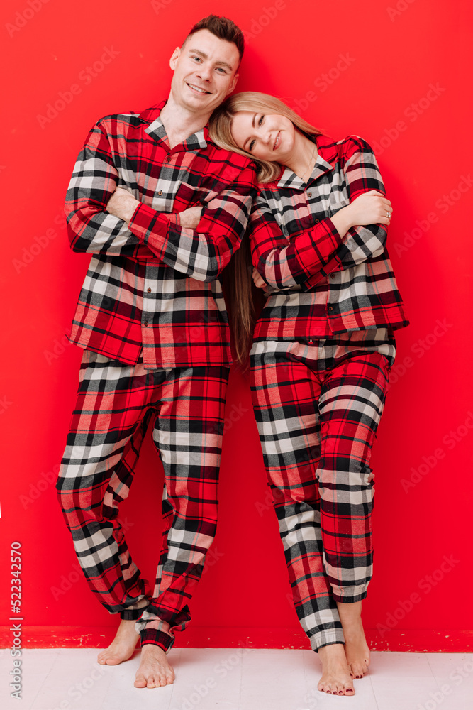 Happy Saint Valentine's Day. Smiling young couple in the same pyjamas having fun on red background. Man and woman in love are enjoying spending time together while celebrating.