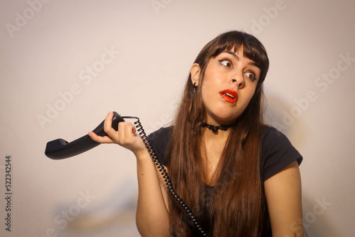 Mujer evade discusión por teléfono, mujer con perforaciones muestra gesto de no oír una llamada por teléfono fijo
