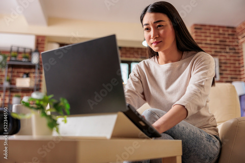 Asian authentic young female freelancer using laptop computer, communicates online web on internet with customer in cozy flat home apartment. Cozy home office workplace, remote work,E learning concept © DC Studio