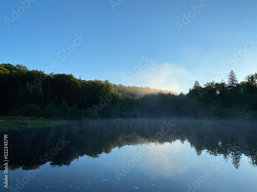 Paysage calme d'une forêt et de l'eau d'une rivière à l'aube. Reflet d'une montagne sur un lac au petit matin. Lever de soleil avec brume sur l'eau.