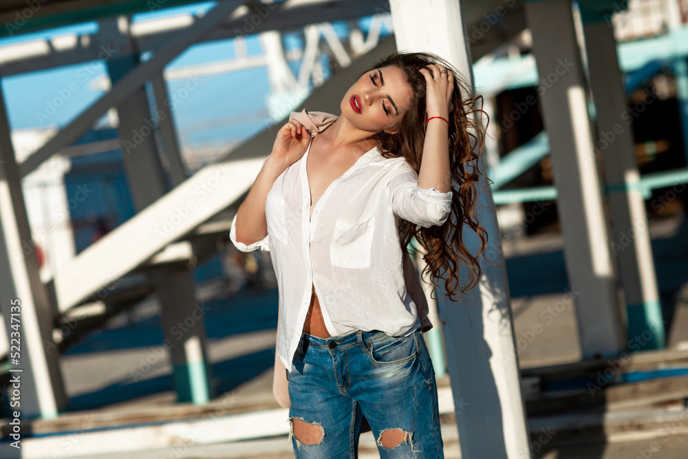 Fashion woman in trendy autumn outfit posing outdoor near see. Vogue style model girl in casual jacket and jeans outdoors. Brunette lady lifestyle portrait.