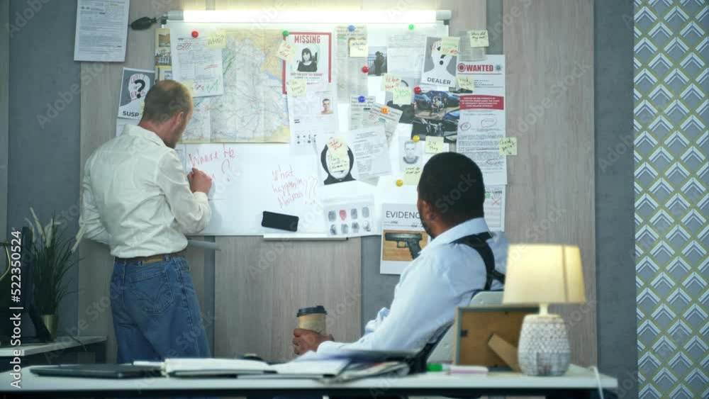 Diverse detectives emotionally discussing and working on crime investigation. Caucasian sergeant writing on crime investigation board to show new evidences and facts to detective at police station. Diverse detectives emotionally discussing and working on crime investigation. Caucasian sergeant writing on crime investigation board to show new evidences and facts to detective at police station.