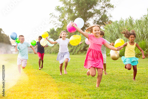 Group of happy kids running through grass with balloons in hands.