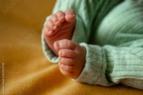 small legs of a newborn baby in green pants on a yellow background. © Vitova Ylia