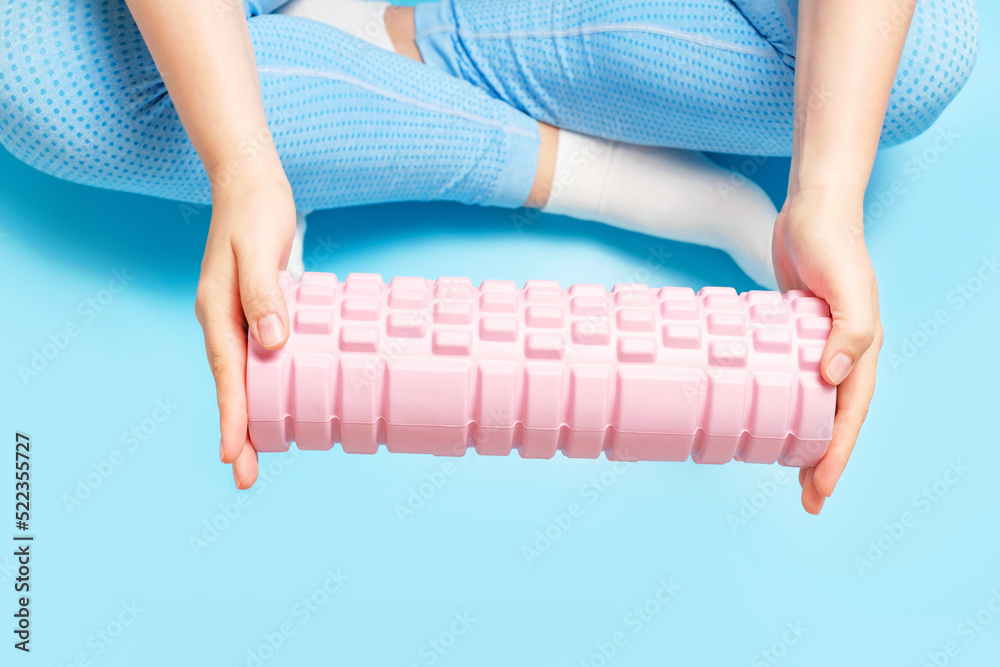 Young woman hold a massage foam roller on blue background close-up, top view.