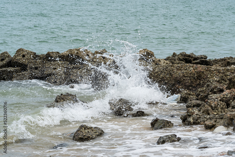 Wave splashes hit the rocks during the low tide of the sea.