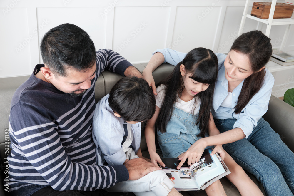 Asian Thai family, adult dad, mum, and children happiness home living relaxing activities and reading book together, leisure on sofa in white room house, lovely weekend, wellbeing domestic lifestyle. Asian Thai family, adult dad, mum, and children happiness home living relaxing activities and reading book together, leisure on sofa in white room house, lovely weekend, wellbeing domestic lifestyle.