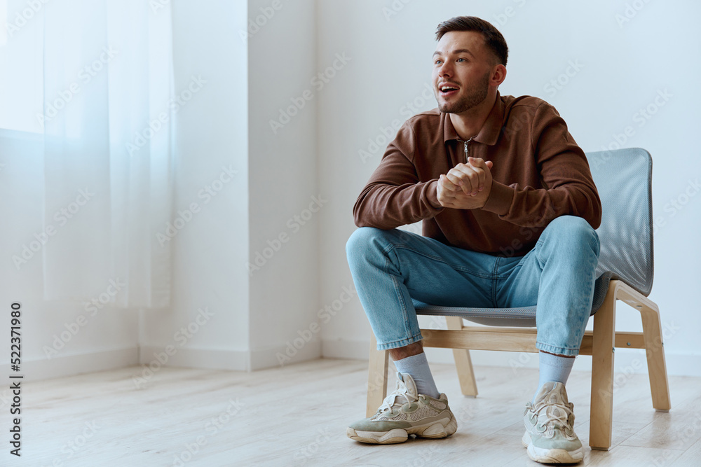Cheerful smiling happy young tanned man fold hands looks aside dreaming about holiday plans cool idea for startup have insight siting in chair at home. People emotions concept. Copy space