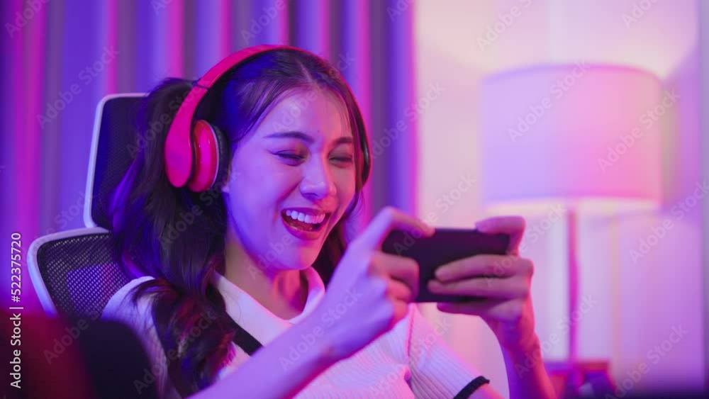 Asian young e-sport woman gamer play online mobile game in neon room.