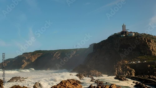 Waves crash over reefs at Die Poort in Mossel Bay, with lighthouse above cave photo