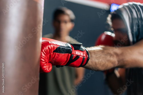 Caucasian man wear boxing gloves punching ahead with trainer in gym. 