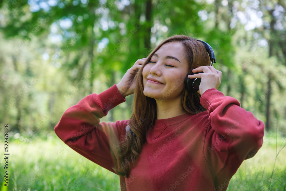 Portrait of a beautiful young asian woman with closed eyes enjoy listening to music with headphone while sitting in the park Portrait of a beautiful young asian woman with closed eyes enjoy listening to music with headphone while sitting in the park