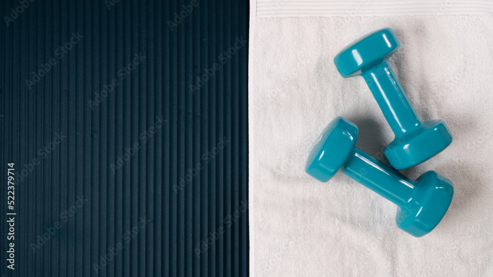 Dumbbells and towel on the workout mat - sports background with space for text Dumbbells and towel on the workout mat - sports background with space for text
