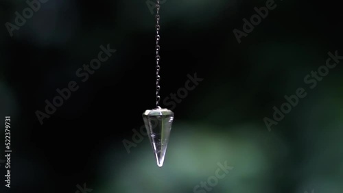 Clear quartz crystal pendulum hanging from Caucasian woman's hands swinging in esoteric and holistic Mystical ritual photo