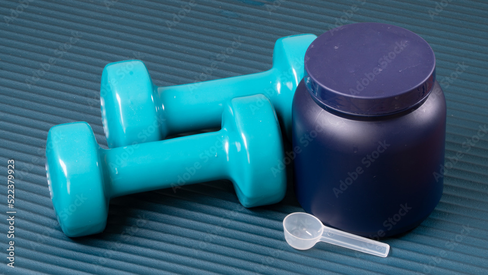 Closed can with sports nutrition, stingy and dumbbells on the mat for training sports background Closed can with sports nutrition, stingy and dumbbells on the mat for training sports background