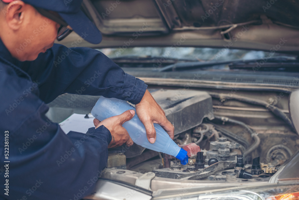 Car Mechanic man hands pouring Deionized purified Distilled water for car battery mechanical service. Close up hands man hold Deionized Distilled liquid water bottle at garage auto mobile car service Car Mechanic man hands pouring Deionized purified Distilled water for car battery mechanical service. Close up hands man hold Deionized Distilled liquid water bottle at garage auto mobile car service