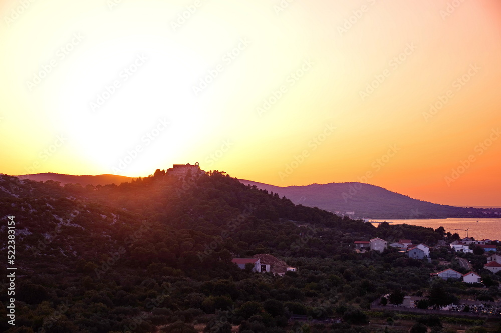 Sunset over monastery on the hill with village on the shore