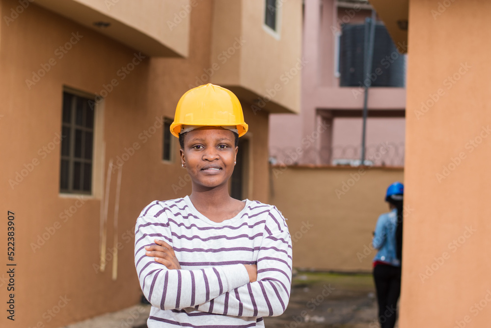 Portrait of an African lady or woman from Nigeria with yellow safety helmet standing outdoor as she represents industrial professionals like construction specialist, builders, architect and engineer Portrait of an African lady or woman from Nigeria with yellow safety helmet standing outdoor as she represents industrial professionals like construction specialist, builders, architect and engineer