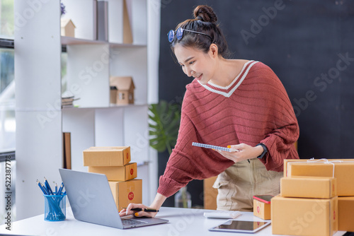 SME Online seller Young Asian woman freelance working on laptop tablet and box, checking online order orders from customers delivery package shipping postal SME entrepreneur online business photo