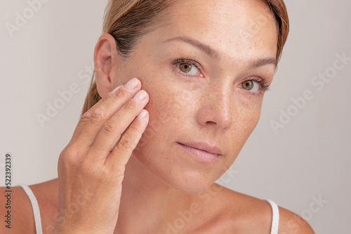 Portrait of cropped caucasian middle aged woman face with freckles touching skin by hand on white background photo
