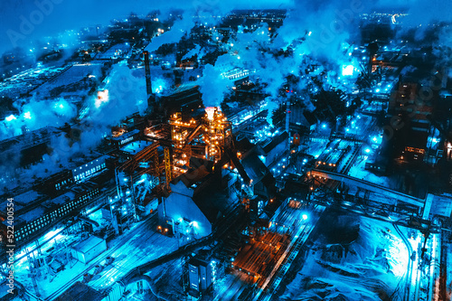 Night top view of steel plant at night with smokestacks and fire blazing out of the pipe. Industrial panoramic landmark with blast furnance of metallurgical production. 