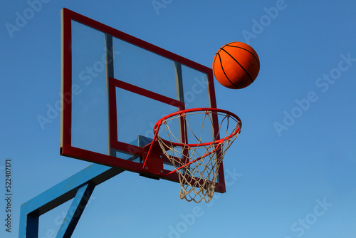 A basketball against the blue sky is flying into the basket.  © BetterPhoto