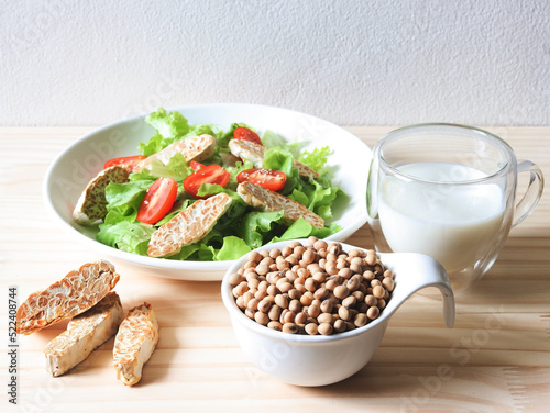 soy bean seeds in white bowl, tempeh in salad dish and soy milk on wooden table, products of soy beans.