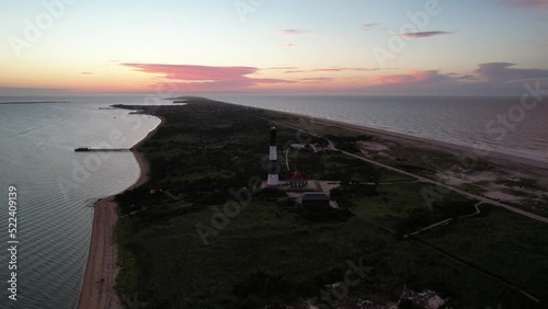 An aerial view of the Fire Island Lighthouse on Long Island, NY. The camera truck left and pan right, orbiting the lighthouse during a colorful sunrise. The light of the lighthouse is on and rotating.