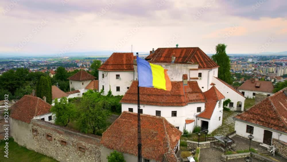 Aerial drone view of The Citadel in Brasov, Romania. Medieval fortress and national flag on the top of a hill. Buildings and green trees around Aerial drone view of The Citadel in Brasov, Romania. Medieval fortress and national flag on the top of a hill. Buildings and green trees around